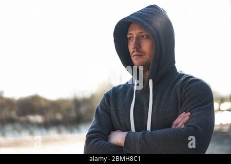 Junge schöne kaukasische Mann dunkelblauen Hoody steht auf der Straße nach einer Jogginghaube. Nahaufnahme Porträt ernst brutal sportlich männlich stehend outsdoo Stockfoto
