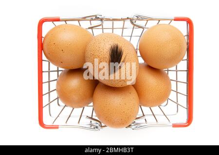 Frische Hühnereier in einem Mini-Warenkorb mit einer kleinen Feder auf der Oberseite isoliert auf weiß. Draufsicht, selektiver Fokus. Stockfoto