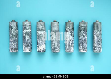 Sieben stark oxidierte AA-Batterien ausgepackt und in einer Reihe auf blauem Hintergrund angeordnet. Stockfoto