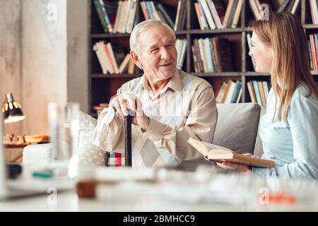 Vater und Tochter zu Hause Bibliothek sitzenden Mann auf Frau, die Buch lachend Stockfoto