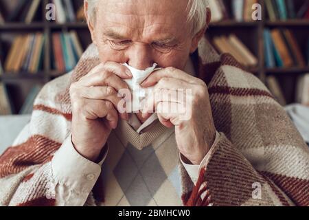 Der ältere Mann allein sitzt in der Bibliothek, bedeckt mit karierten Niesen aus nächster Nähe Stockfoto