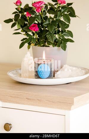 Brennende Glaskerze mit selbstgemachtem Schild, das das Symbol Blume des Lebens im Inneren mit Halbedelstein-Geoden zeigt. Spirituelle Symbole zu Hause. Stockfoto