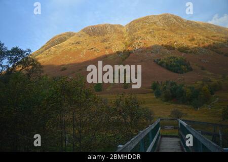 Fußgängerbrücke über den Fluss Nevis und die Hänge des Bades von Ben Nevis in spätnachmittäglichen Herbstsonnen Stockfoto