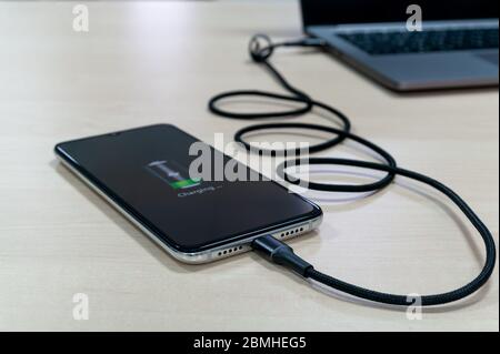 Moderne Smartphones laden vom Laptop auf einen hellen Holztisch. Modernes Technologiekonzept. Selektiver Fokus Stockfoto