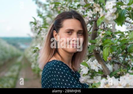 Ein schönes und charmantes Mädchen steht in der Nähe eines blühenden Baumes. Schöne Mädchen Gesicht Nahaufnahme. Stockfoto