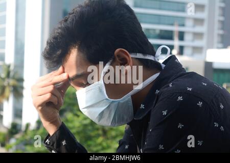 Schöner junger Mann mit kalter Grippe Gefühl Kopfschmerzen. Er trägt eine Operationsmaske und fühlt sich auch im Quarantäneleben zu Hause gestresst. Stockfoto