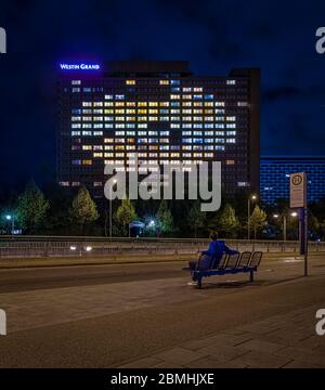 Mann sitzt auf einer Bank und beobachtet die herzförmigen, beleuchteten Fenster des Grand Westin Hotels in München. Deutschland am 14. april 2020 symbolisiert Stockfoto