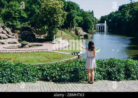 Sofia Park, Ukraine. Junge Frau mit einer touristischen Karte Spaziergänge in einem Landschaftsgarten. Mädchen mit einer touristischen Karte auf dem Hintergrund des Sees mit einem Brunnen. Stockfoto