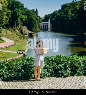 Sofia Park, Ukraine. Junge Frau mit einer touristischen Karte Spaziergänge in einem Landschaftsgarten. Mädchen mit einer touristischen Karte auf dem Hintergrund des Sees mit einem Brunnen. Stockfoto