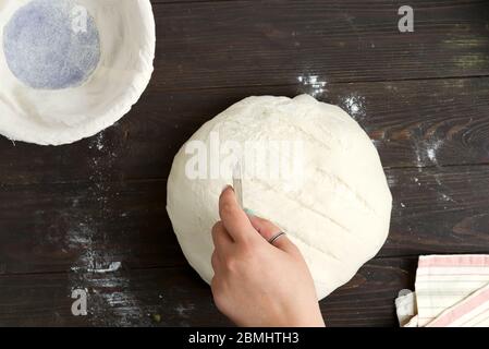 Prozess Backen hausgemachte gesundes Brot mit Frau Hand Schneidelinien auf einem frisch zubereiteten Laib auf einem dunklen Holzhintergrund, kopieren Raum. Schritt für Schritt Stockfoto