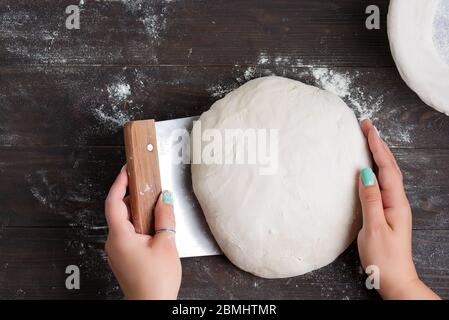 Frisch gekochter Teig und Schaber in der Hand einer Frau. Prozess der Vorbereitung von hausgemachtem Brot auf einem dunklen Holzhintergrund, kopieren Raum. Schritt für Schritt. Stockfoto