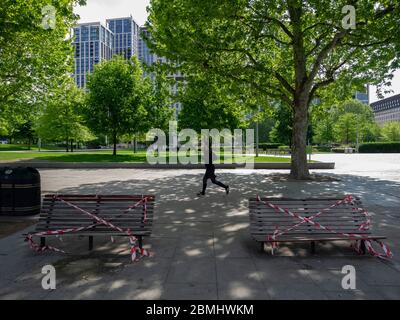 London. GROSSBRITANNIEN. Mai 2020 um 10:30 Uhr. Foto eines Mannes, der während der Lockdown in Jubilee Gardens, South Bank, läuft. Auf dem Foto zwei Bänke mit Stockfoto