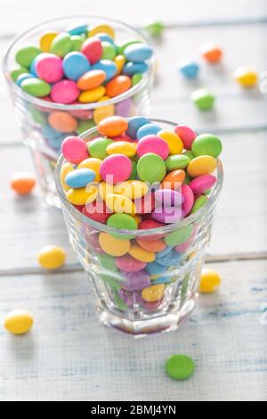 Zwei Gläser voll von süßen runden bunten Leckereien, von denen einige aus dem Glas auf einem weißen Tisch gefallen sind. Stockfoto