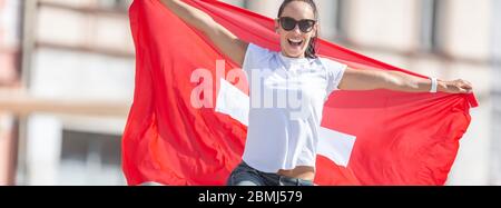 Schweizer Fan feiert auf einer Straße mit einer Fahne hinter sich. Stockfoto