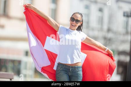 Schweizer Fan hält eine Flagge auf einer Straße und lächelt an einem sonnigen Tag. Stockfoto