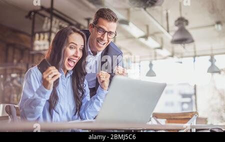 Geschäftsfrau und Geschäftsmannes Kollegen feiern einen Erfolg mit begeisterten Gesichtsausdrücken, die auf dem Notebook-Bildschirm schauen. Stockfoto