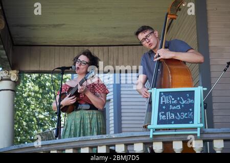 Attraktive junge Retro-Paar singen und spielen Kontrabass und Ukulele zu einer Menge im Freien bei einem Sommer Veranda Konzert-Event in einer historischen Residenz Stockfoto