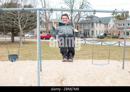 Seltsame bizarre exzentrische Menschen Konzept. Erwachsener Mann in Vintage teure modische Stiefel Reiten auf einer Schaukel in Stadtpark auf Spielplatz für Kinder Stockfoto