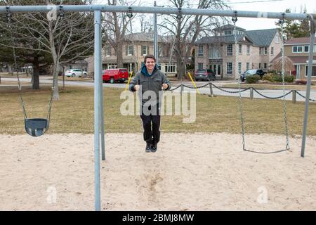 Seltsame bizarre exzentrische Menschen Konzept. Erwachsener Mann in Vintage teure modische Stiefel Reiten auf einer Schaukel in Stadtpark auf Spielplatz für Kinder Stockfoto