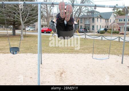 Seltsame bizarre exzentrische Menschen Konzept. Erwachsener Mann in Vintage teure modische Stiefel Reiten auf einer Schaukel in Stadtpark auf Spielplatz für Kinder Stockfoto