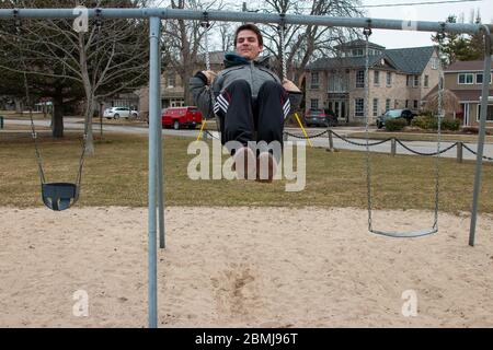 Seltsame bizarre exzentrische Menschen Konzept. Erwachsener Mann in Vintage teure modische Stiefel Reiten auf einer Schaukel in Stadtpark auf Spielplatz für Kinder Stockfoto