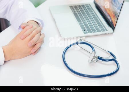 Mediziner arbeitet am Schreibtisch. Nahaufnahme des Stethoskops. Arzt Mann Videoanruf sitzen Hand in Hand und hören Patienten erklären auf der Vorderseite Laptop Comput Stockfoto