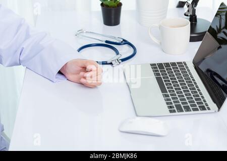 Mediziner arbeitet am Schreibtisch. Nahaufnahme des Stethoskops. Hand der asiatischen Frau Arzt erklären, um Patienten auf dem Tisch vor Laptop-Computer an der hos Stockfoto