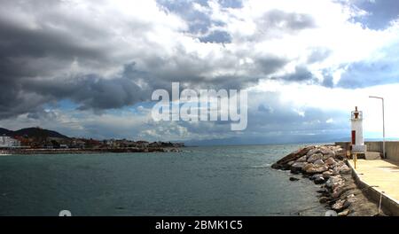 Ein Hafen aus Felsen und ein weißer Leuchtturm. Welliges Meer und wolkiges windiges Wetter. Stockfoto