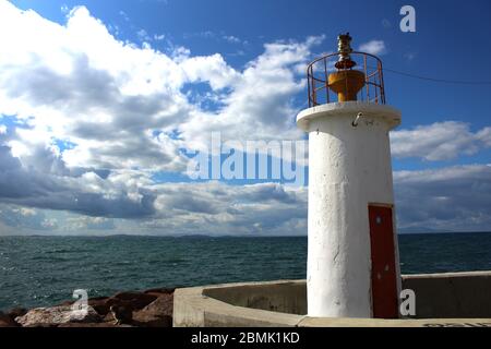 Ein Hafen aus Felsen und ein weißer Leuchtturm. Welliges Meer und wolkiges windiges Wetter. Stockfoto