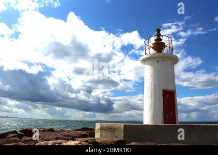 Ein Hafen aus Felsen und ein weißer Leuchtturm. Welliges Meer und wolkiges windiges Wetter. Stockfoto