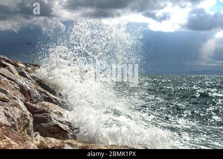 Ein Hafen aus Felsen und ein weißer Leuchtturm. Welliges Meer und wolkiges windiges Wetter. Stockfoto