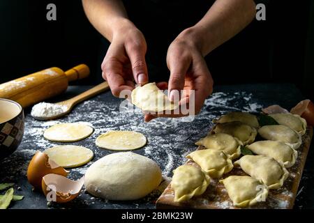 Kochen Sie in der dunklen Jacke bereitet Knödel. Über dem dunklen Tisch, auf dem die fertigen Knödel gelegt sind. Vorderansicht, Nahaufnahme Stockfoto