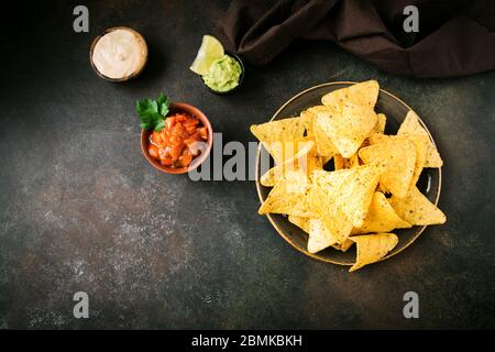 Mexikanische Mais-Chips Nachos und Satz von traditionellen Dips, Draufsicht, Kopierraum. Tortilla oder Nacho Chips mit Saucen für den Snack. Stockfoto