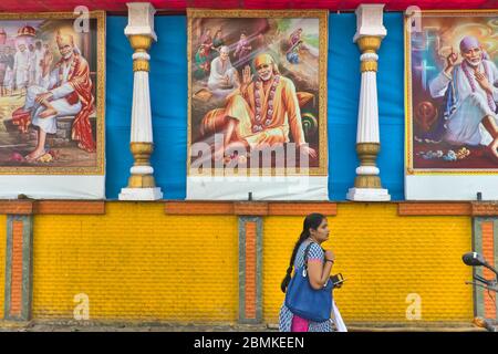 Eine Frau in Mumbai, Maharashtra, Indien, passiert eine blau-gelbe Wand mit drei Wandmalereien des Hindu-heiligen Sai Baba von Shirdi (1838-1918) Stockfoto