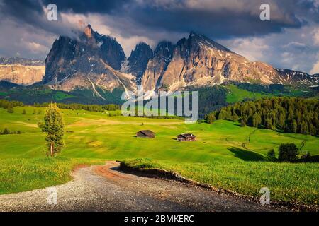 Atemberaubender Sommer-Alpenort mit Holzhütten, Landstraße und verschneiten Bergen bei Sonnenuntergang, Dolomiten, Seiser Alm Resort, Italien, Europa Stockfoto