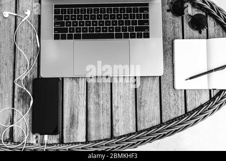 Schwarz-weiß Foto von oben eines Arbeitsbereichs mit Laptop, auf einem Holztisch mit Smartphone und einem Notebook für die Aufnahme von Koffern. Business con Stockfoto