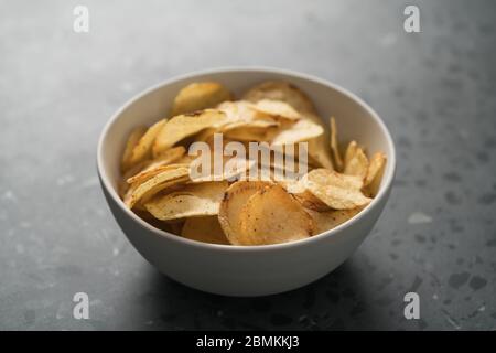 Kartoffelchip leicht mit schwarzem Pfeffer in einer weißen Schüssel bestreut Auf konkretem Hintergrund Stockfoto