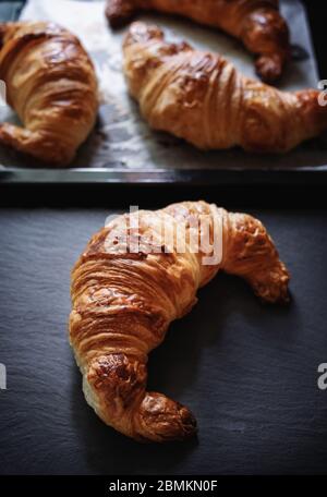 Frisch gebackene Croissants auf schwarzem Steinteller und schwarzem Tablett Stockfoto