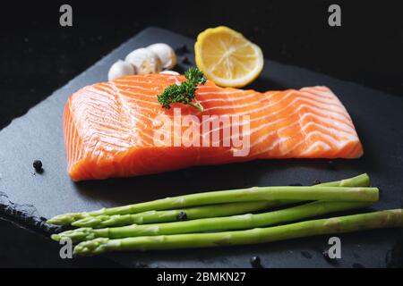 Frische rohe Lachsscheibe mit Kraut und Zutaten, auf schwarzem Schieferteller. Lachsfilet Stockfoto