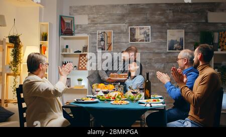 Frau und Abendessen mit Freunden und Familie mit einer Überraschung mit Kuchen. Sie bläst die Kerzen. Zeitlupe aufgenommen Stockfoto