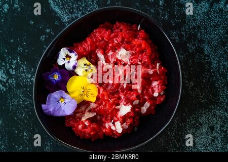 Risotto mit essbaren Blumen und Parmesan aus Bio-Rüben in schwarzer Keramikschale. Gesunde Bio-Lebensmittel. Stockfoto