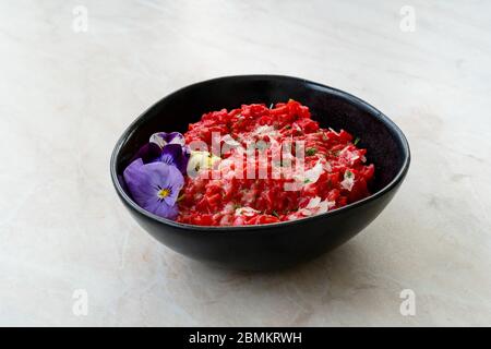 Risotto mit essbaren Blumen und Parmesan aus Bio-Rüben in schwarzer Keramikschale. Gesunde Bio-Lebensmittel. Stockfoto