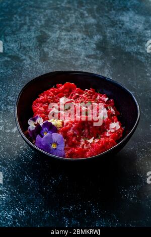 Risotto mit essbaren Blumen und Parmesan aus Bio-Rüben in schwarzer Keramikschale. Gesunde Bio-Lebensmittel. Stockfoto