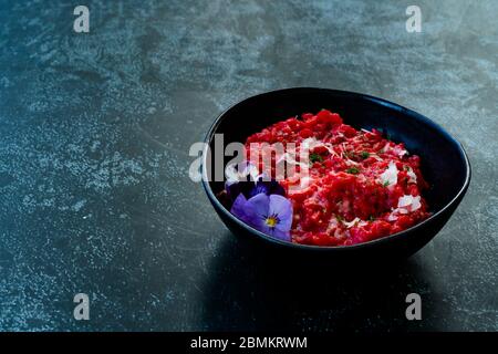 Risotto mit essbaren Blumen und Parmesan aus Bio-Rüben in schwarzer Keramikschale. Gesunde Bio-Lebensmittel. Stockfoto