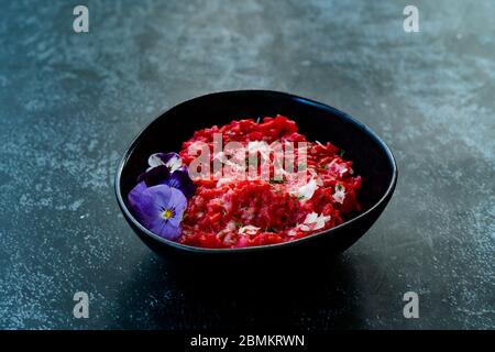 Risotto mit essbaren Blumen und Parmesan aus Bio-Rüben in schwarzer Keramikschale. Gesunde Bio-Lebensmittel. Stockfoto