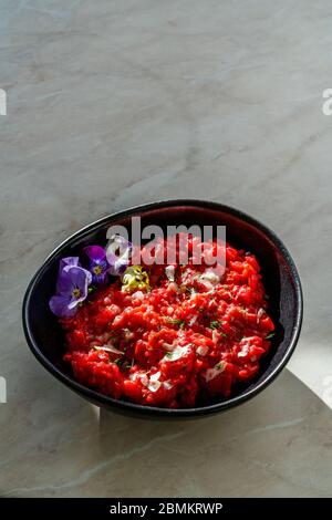 Risotto mit essbaren Blumen und Parmesan aus Bio-Rüben in schwarzer Keramikschale. Gesunde Bio-Lebensmittel. Stockfoto