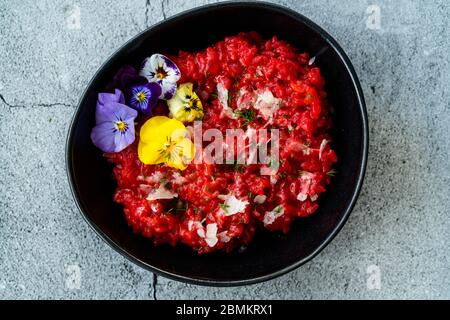 Risotto mit essbaren Blumen und Parmesan aus Bio-Rüben in schwarzer Keramikschale. Gesunde Bio-Lebensmittel. Stockfoto