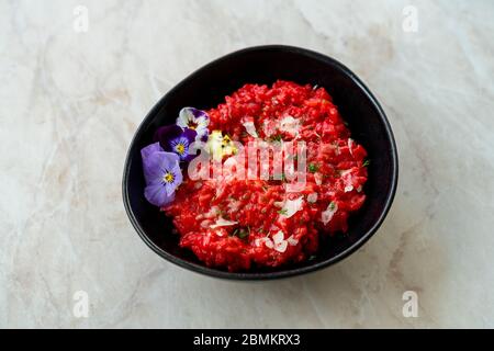 Risotto mit essbaren Blumen und Parmesan aus Bio-Rüben in schwarzer Keramikschale. Gesunde Bio-Lebensmittel. Stockfoto