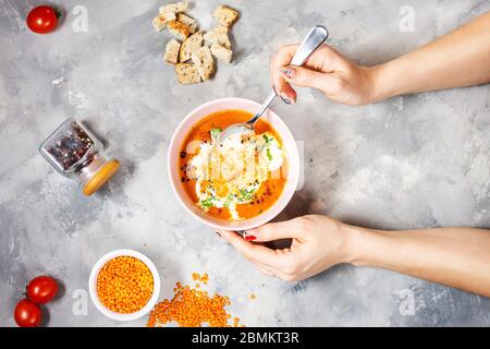 Köstliche Linsensuppe mit schwerer Sahne auf Betontisch mit roter Paprika, Brot-Toasts. Weibliche Hände hält einen Löffel. Draufsicht Stockfoto