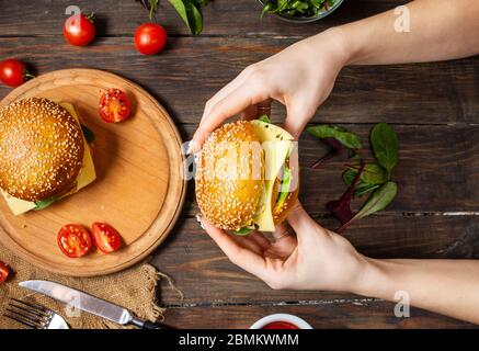 Weibliche Hände halten einen Burger mit Huhn, frittiertem Ei und Käse auf einem rustikalen Holzhintergrund. Draufsicht Stockfoto